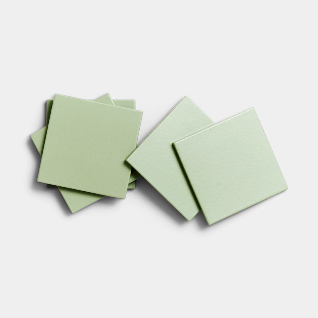 Four Eucalyptus 4x4 matte ceramic tiles by Zia Tile are stacked and slightly overlapping on a plain white background, highlighting the simple elegance of these light green ceramics.