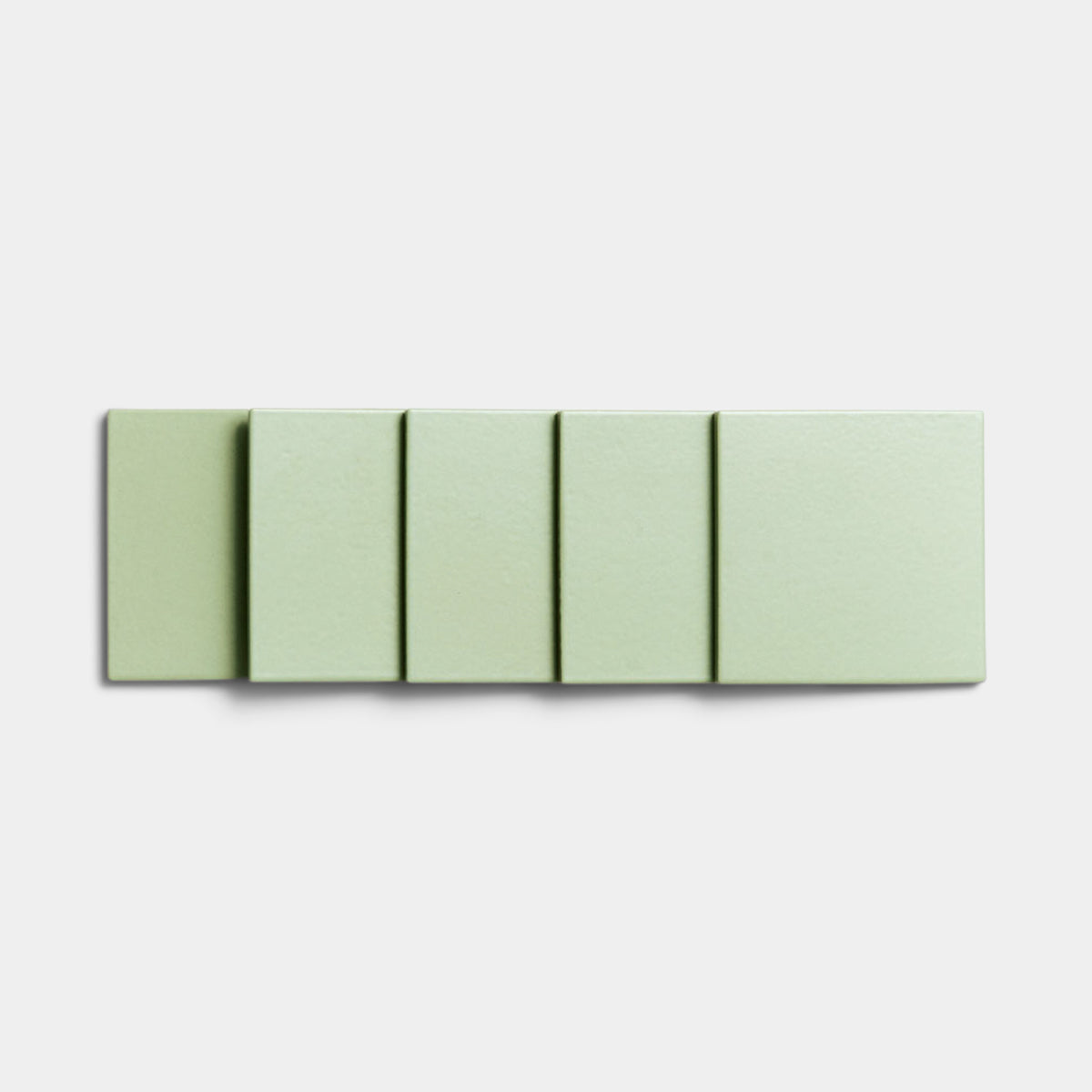Five Eucalyptus 4x4 ceramic tiles by Zia Tile, featuring a light green matte finish, are arranged in a row on a white background. Each tile is identical in color and size, forming a minimalistic, geometric display.