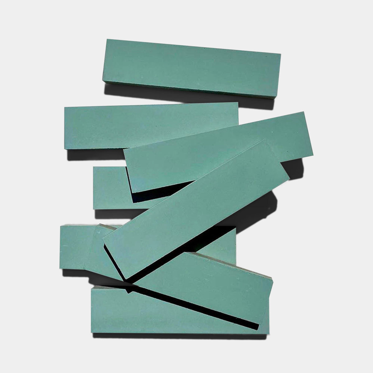 Several rectangular, flat Everglade 2x8 ceramic tiles by vendor-unknown, in a teal hue, are stacked in a scattered arrangement on a light gray background.