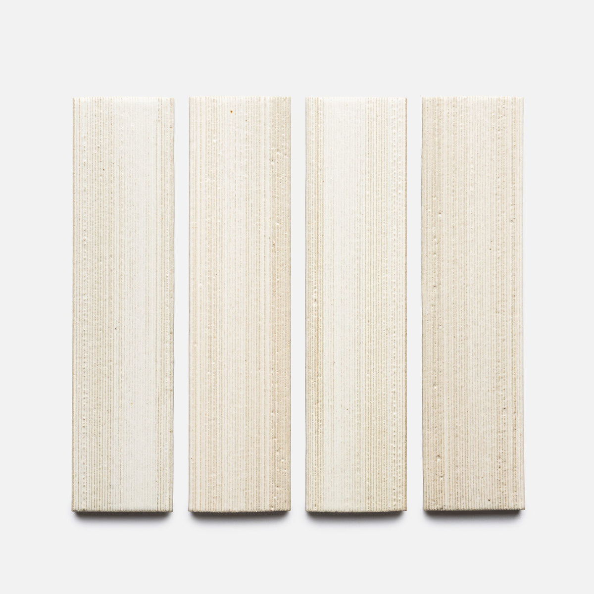 Four Feather + Etched, Sample tiles by Zia Tile are arranged vertically on a light gray background. The rectangular beige tiles feature a subtle linear pattern with slight variations in shade and texture.