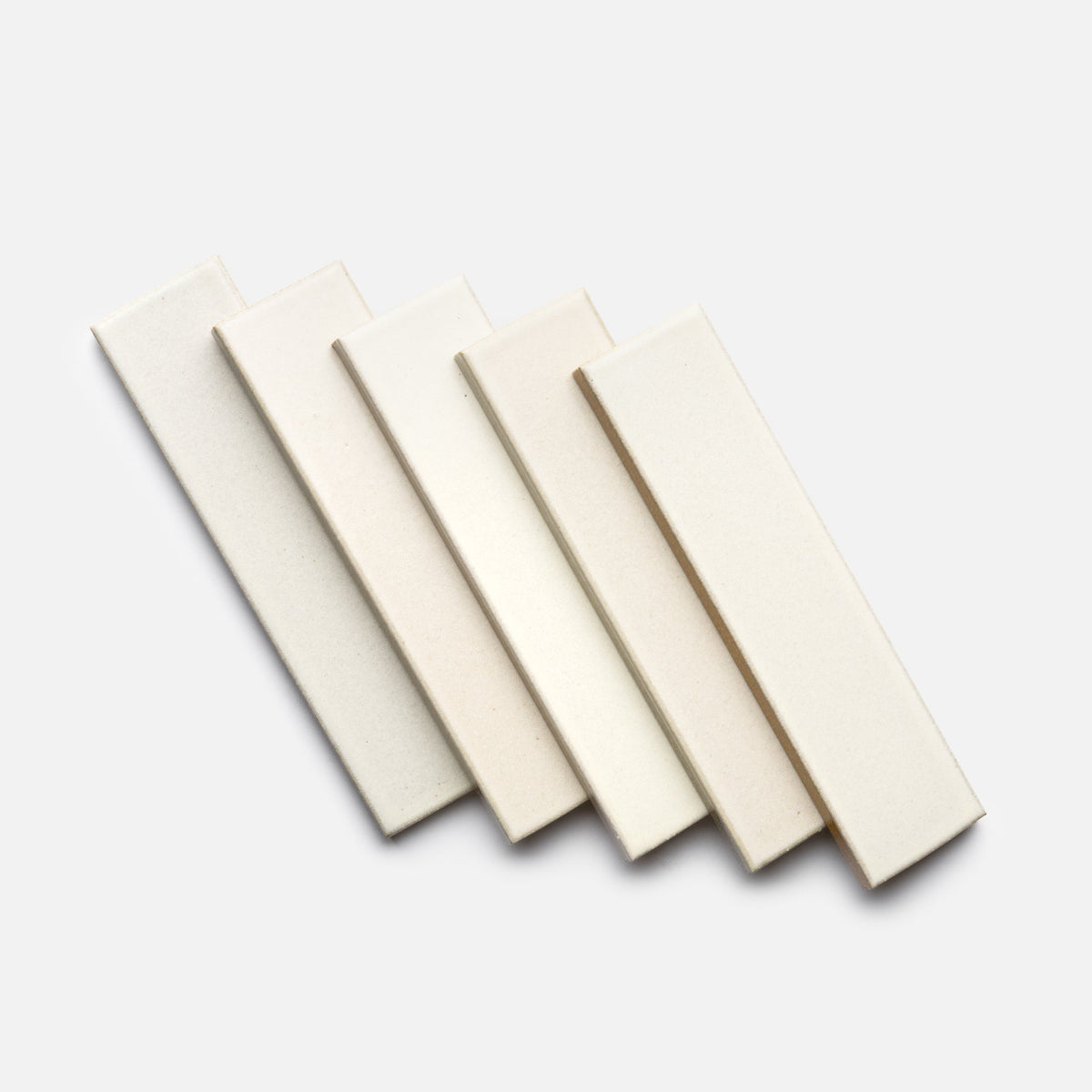 Five rectangular Feather + Flat samples by Zia Tile, in creamy off-white ceramic, are arranged in a slightly fanned-out pattern on a light background. Each tile shows subtle variations in shade and is similar in size and color.