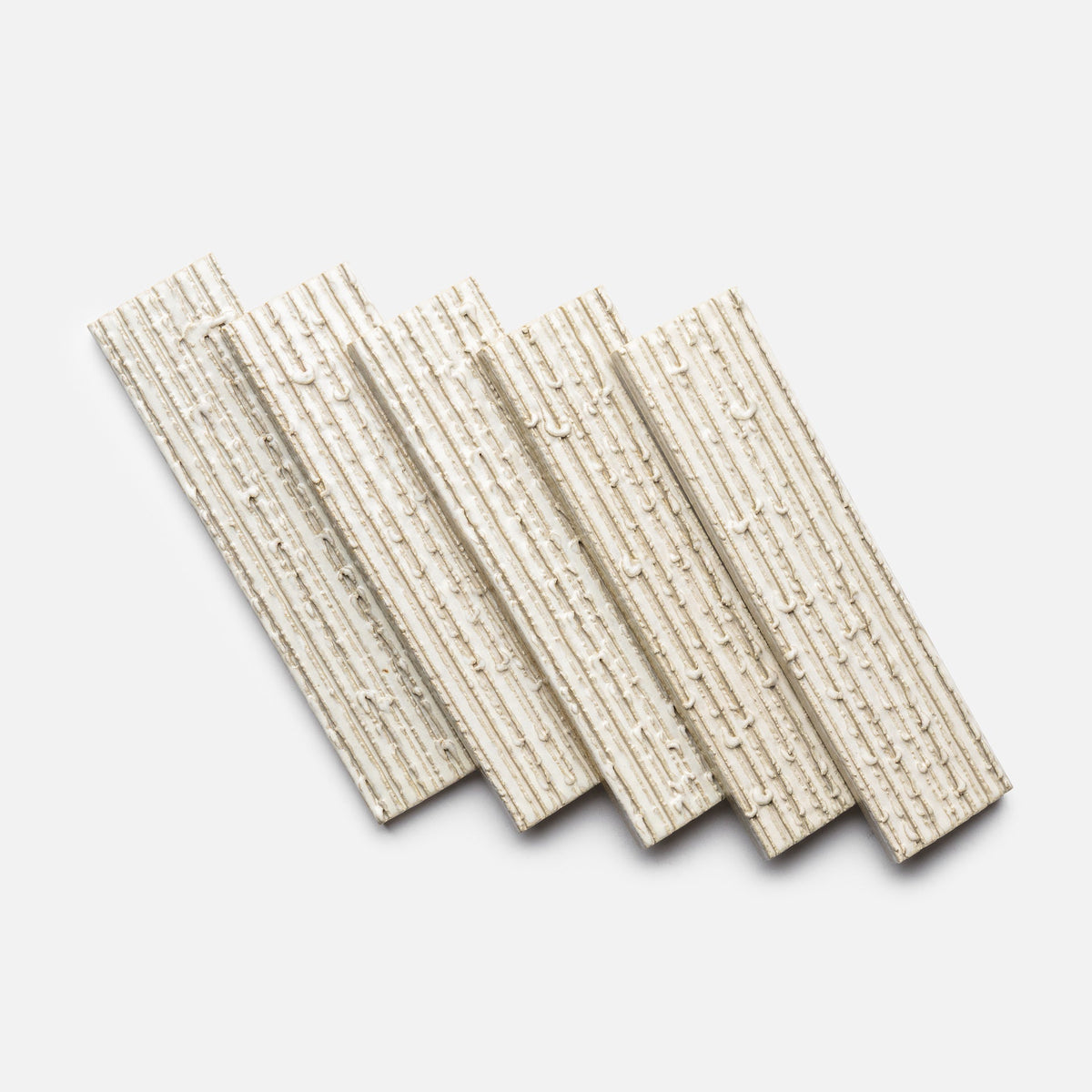 Five Feather + Furrowed tiles by Zia Tile, with a ridged and textured rectangular design, are arranged in a slightly overlapping diagonal pattern on a white background.