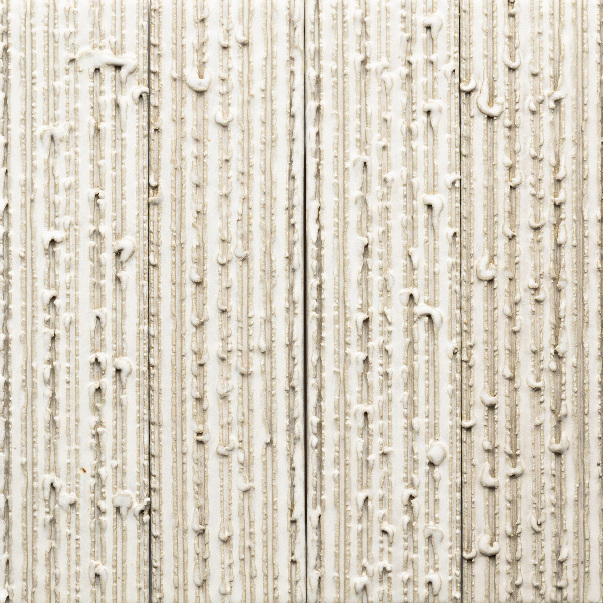 Close-up of Feather + Furrowed, Sample by Zia Tile—textured beige wall tile with vertical ridges and irregular white lines of thick adhesive, forming a rough, uneven surface pattern.
