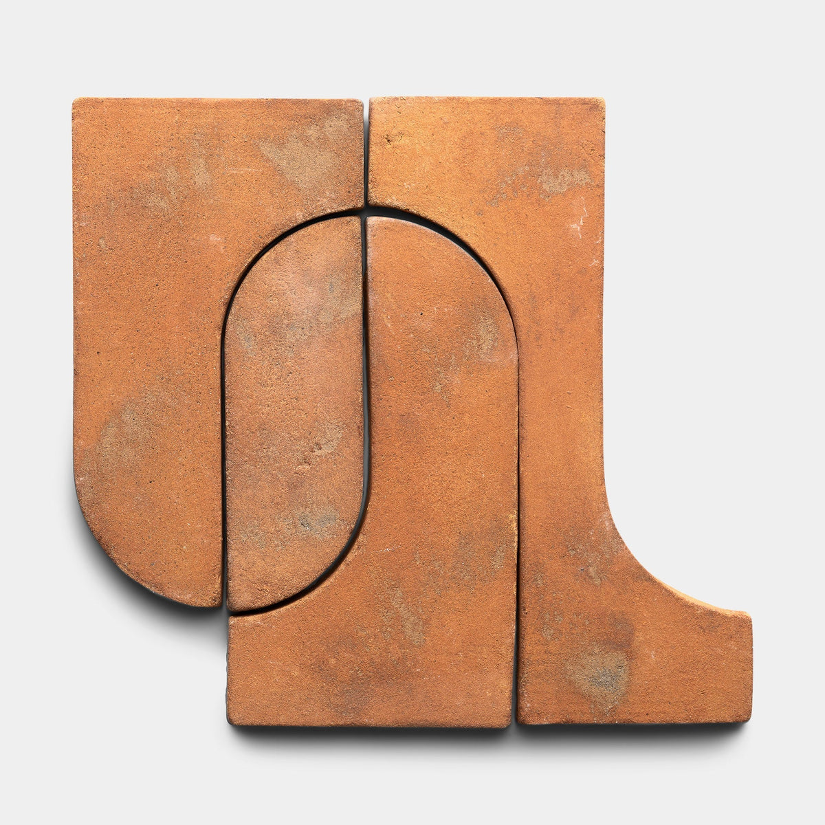 Three Durango + Fired Earth clay tiles from Zia Tile, in terracotta tones and smooth finishes, are arranged in an abstract geometric pattern of curves and straight lines on a light gray background.