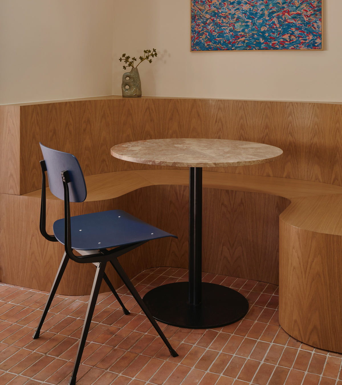 A cozy corner features a Zia Tile 2x6 Rectangle + Fired Earth tile, a black-based round table, dark blue chair, built-in wood bench, terra cotta accents, and a flower vase—evoking San Miguel de Allende’s charm.