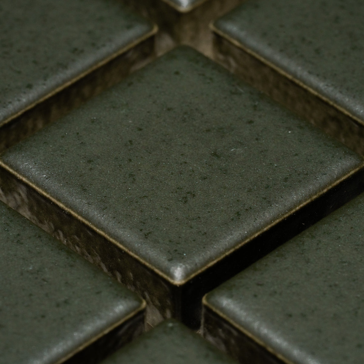Close-up of Zia Tile's Fraser 1x1: dark green, square ceramic tiles with slightly rounded edges, visible grout lines, and a smooth matte finish featuring subtle speckles, arranged in a grid pattern.