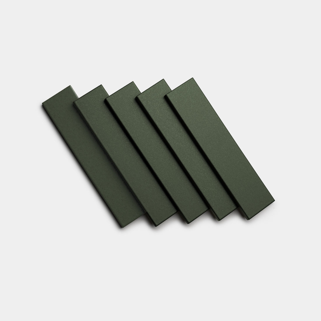 Five Fraser 2x8 tiles by Zia Tile, in dark green, are arranged in a slightly overlapping, fanned-out pattern on a plain white background.