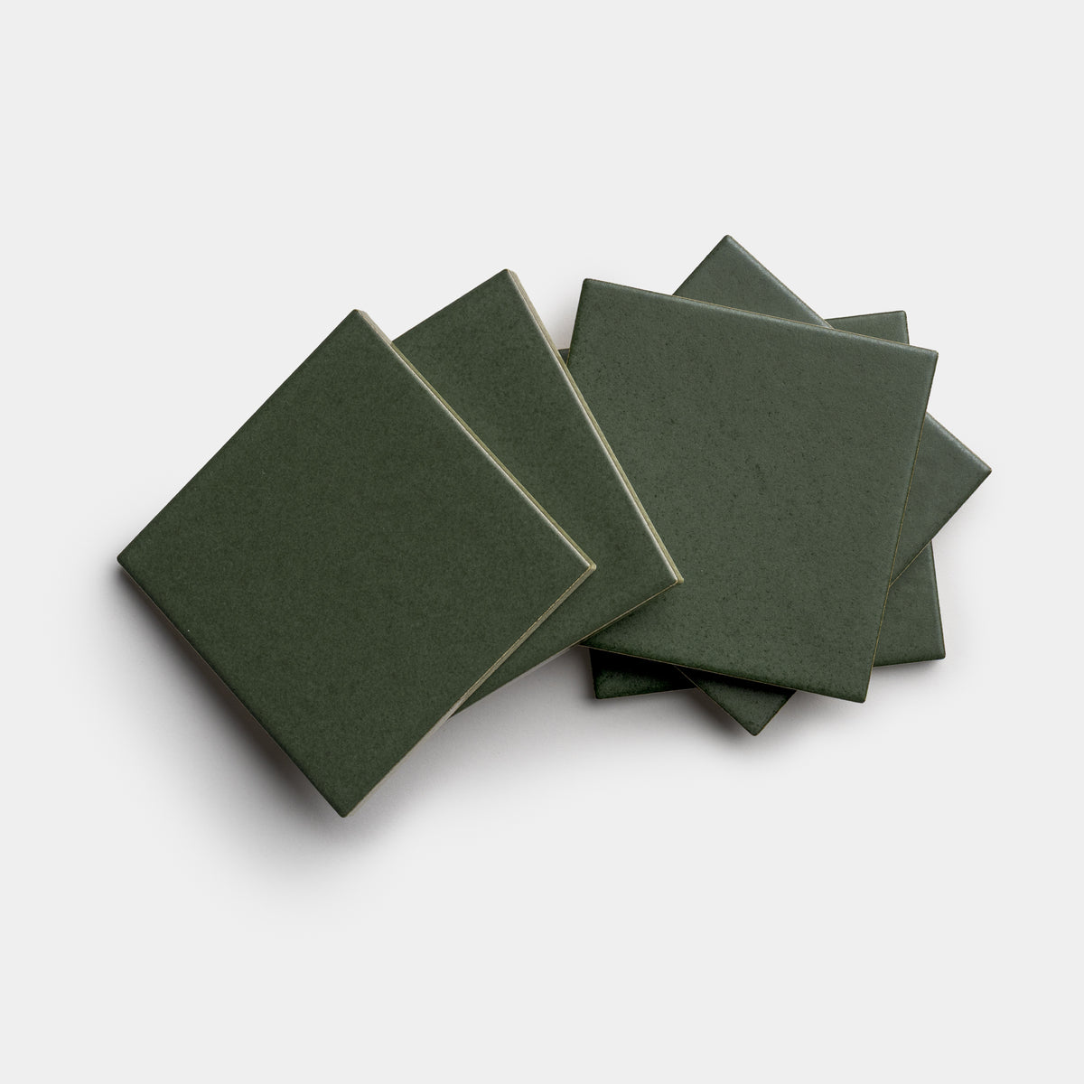 Five Fraser 4x4 square ceramic tiles by Zia Tile in dark green are stacked and slightly fanned out on a plain white background.