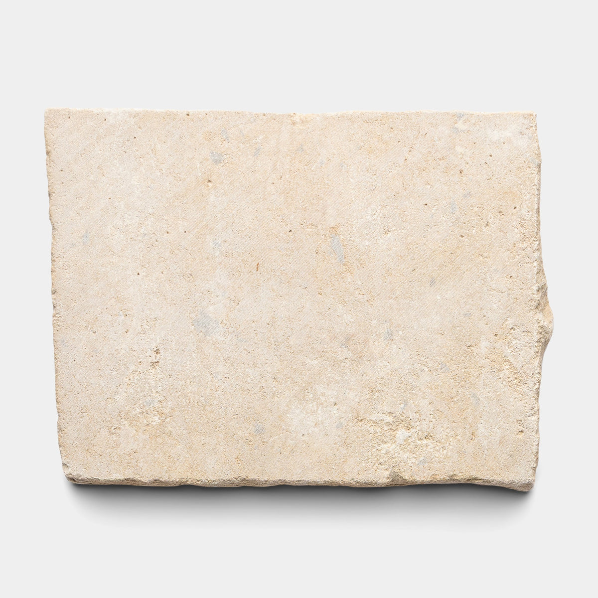 A rectangular French Cobblestone sample by Zia Tile in beige with a rough, uneven texture and a slightly chipped edge, displayed against a plain white background.