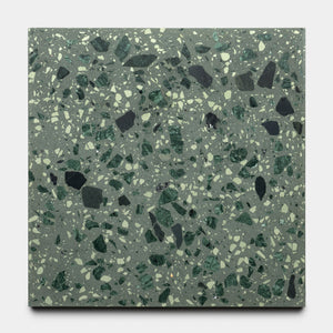 The Gaia 12x12 by Zia Tile is a square terrazzo tile with a greenish-gray base, accented by dark and light green stone chips of various sizes and shapes throughout its surface.