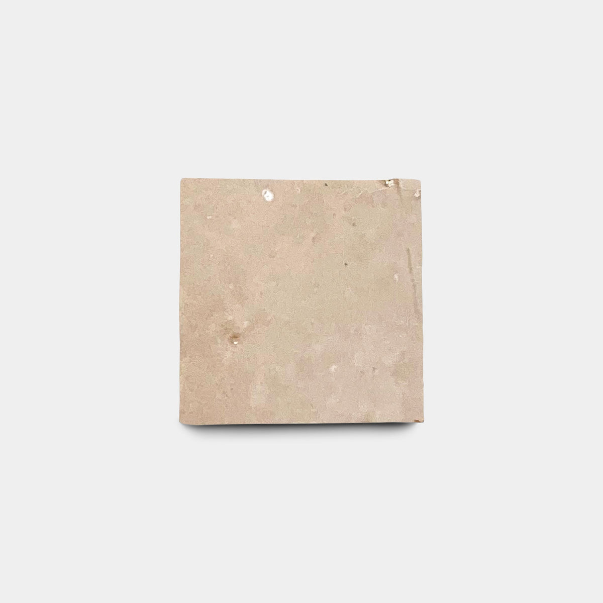 A single, square Glazed Earth 2x2 sample tile from Zia Tile, beige with minor imperfections and a slightly rough surface, is set against a plain white background to showcase its artisanal quality.