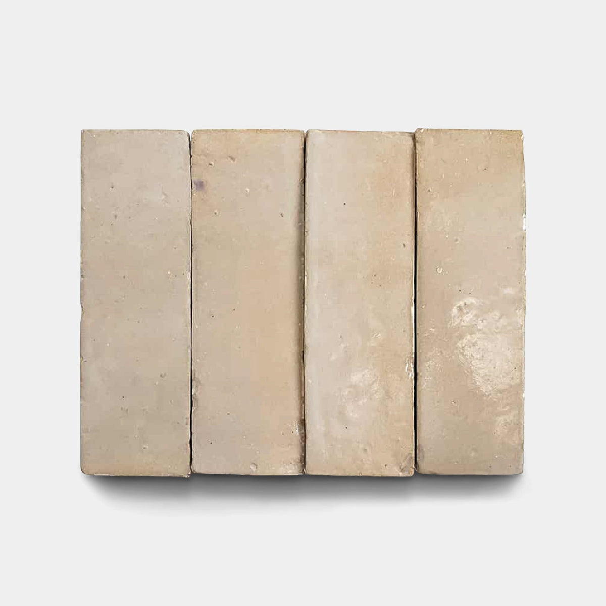 Four square, light beige Glazed Earth 2x2 sample tiles by Zia Tile are arranged side by side on a plain white background, casting faint shadows beneath them.