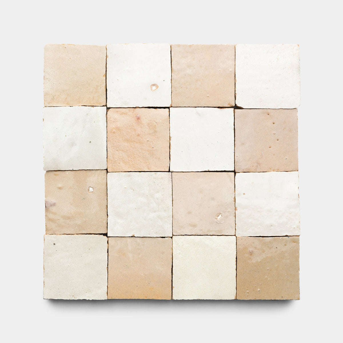 A 4x4 square grid of Zia Tile’s Glazed Earth + Casablanca Checkerboard samples, each handmade ceramic tile in neutral beige, cream, and light brown tones is uniquely shaded.