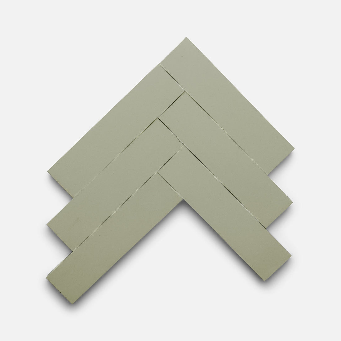 Five rectangular, pale green Gypsum 2x8 tiles by Zia Tile are arranged in a herringbone pattern on a plain white background.