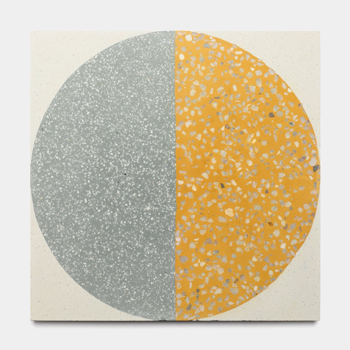 The Highball Cadmium 12x12 sample by Zia Tile is a square cement tile featuring a large central circle split vertically—gray with white speckles on the left, and yellow with gray and white speckles on the right, for a bold modern look.
