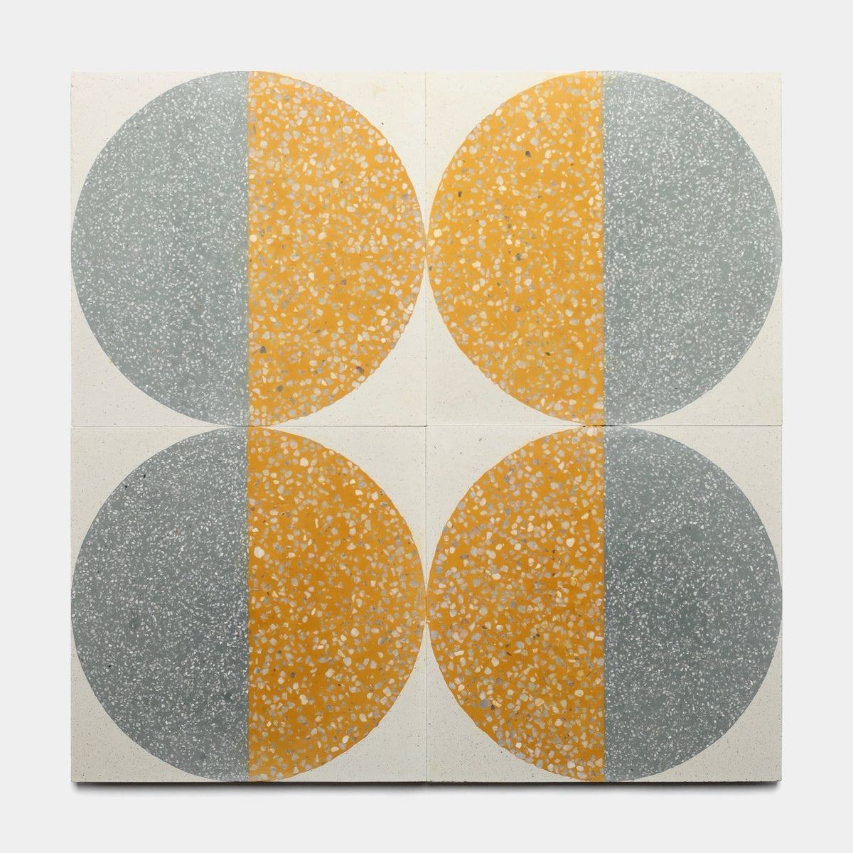Four Highball Cadmium 12x12 tiles by Zia Tile arranged in a grid, each showing a circle split vertically into yellow speckled and gray speckled halves, creating a symmetrical pattern inspired by handmade tile artistry.