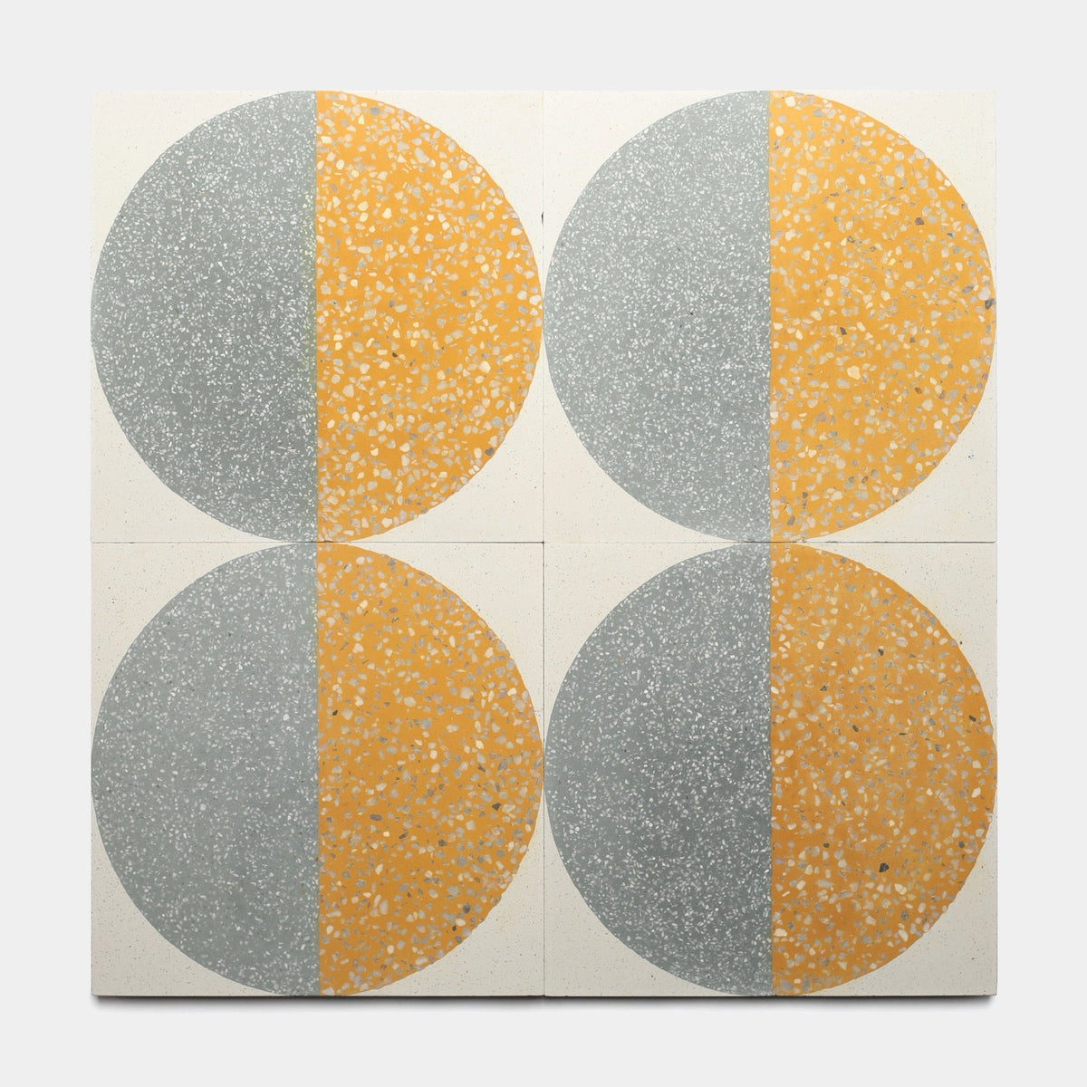Four handmade Highball Cadmium 12x12 tiles from Zia Tile are set in a grid. Each has a large circle split vertically—speckled gray on the left, yellow on the right—on a light background, showcasing their artisanal cement tile style.
