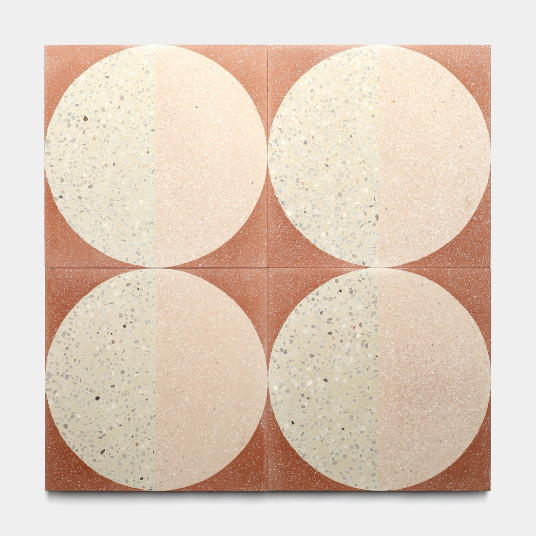 Four handmade Highball Jaipur Pink 12x12 tiles by Zia Tile, each with a vertically bisected cream and beige circle on a reddish-brown background, offer a modern cement tile look. Sample size available.