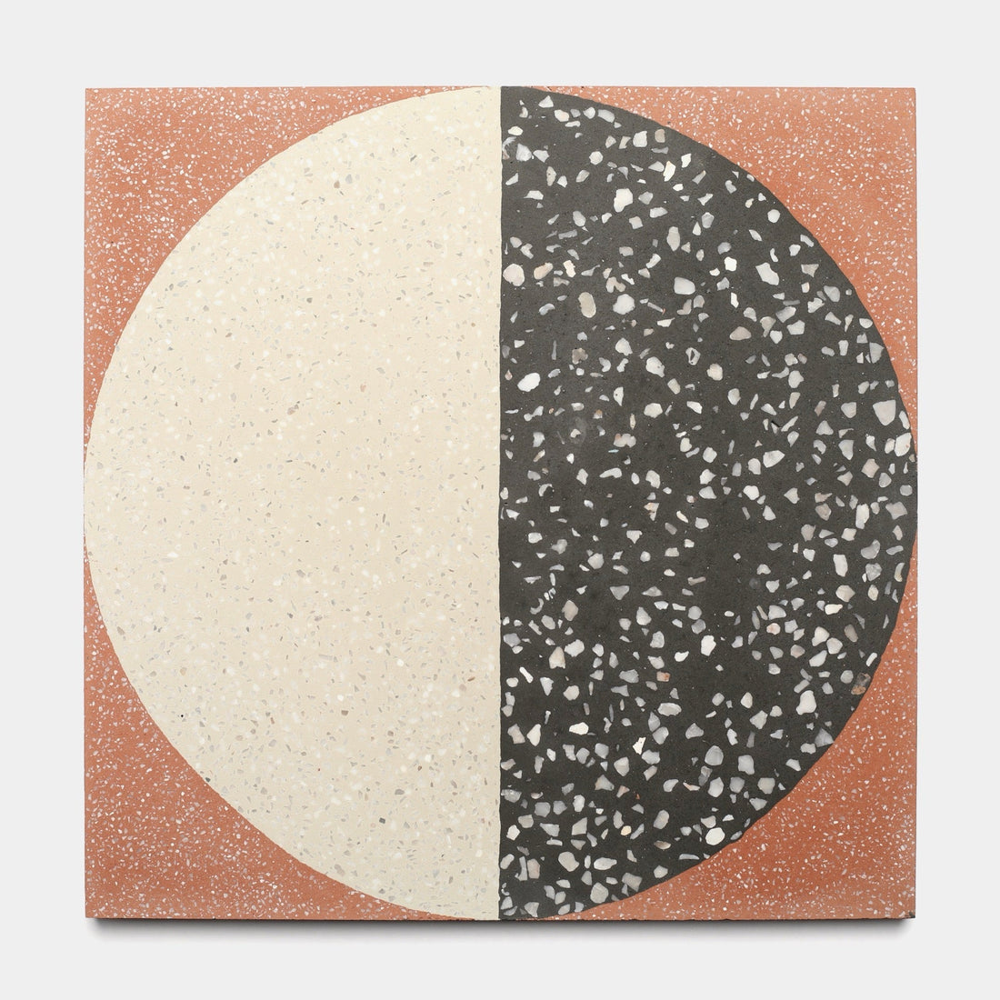 The Zia Tile Highball Rust 12x12 sample is a square handmade tile with a large circle split vertically: cream with light specks on the left, black with white specks on the right, set on a terracotta background dusted with tiny white flecks.