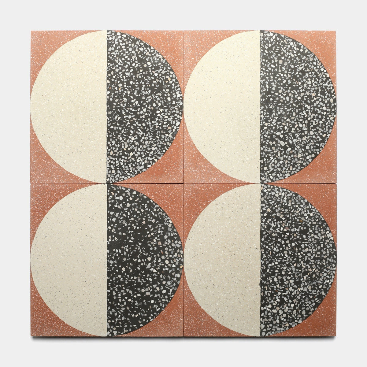 Four Zia Tile Highball Rust 12x12 samples arranged in a grid, each with a large circle split vertically—one half solid cream, the other speckled black and white—on a muted terracotta background.