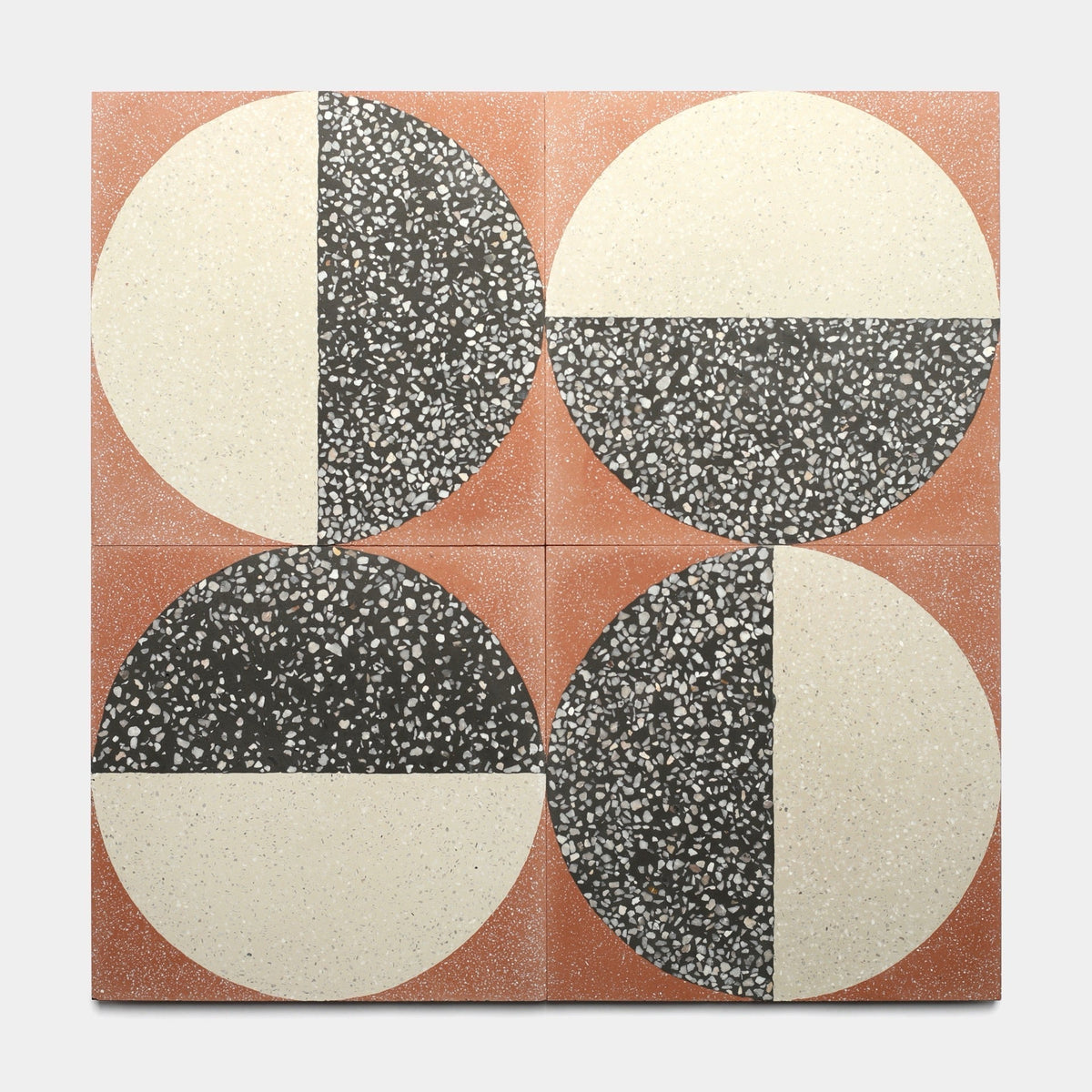 Four Highball Rust 12x12 sample tiles by Zia Tile, each with a large circle split between light cream and dark speckled halves, accent an artisanal reddish-brown terrazzo-like background with handcrafted cement tile charm.