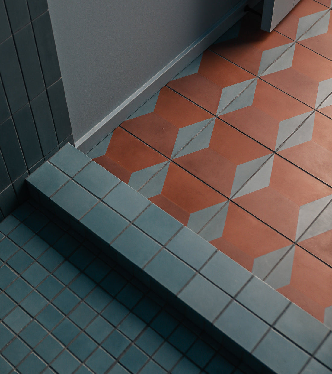 The lower floor has small square blue tiles; the upper step uses Zia Tile's Colorama Tyrian 8x8 handmade tiles—orange with a blue and white geometric diamond pattern. Walls are tiled in blue and painted white.