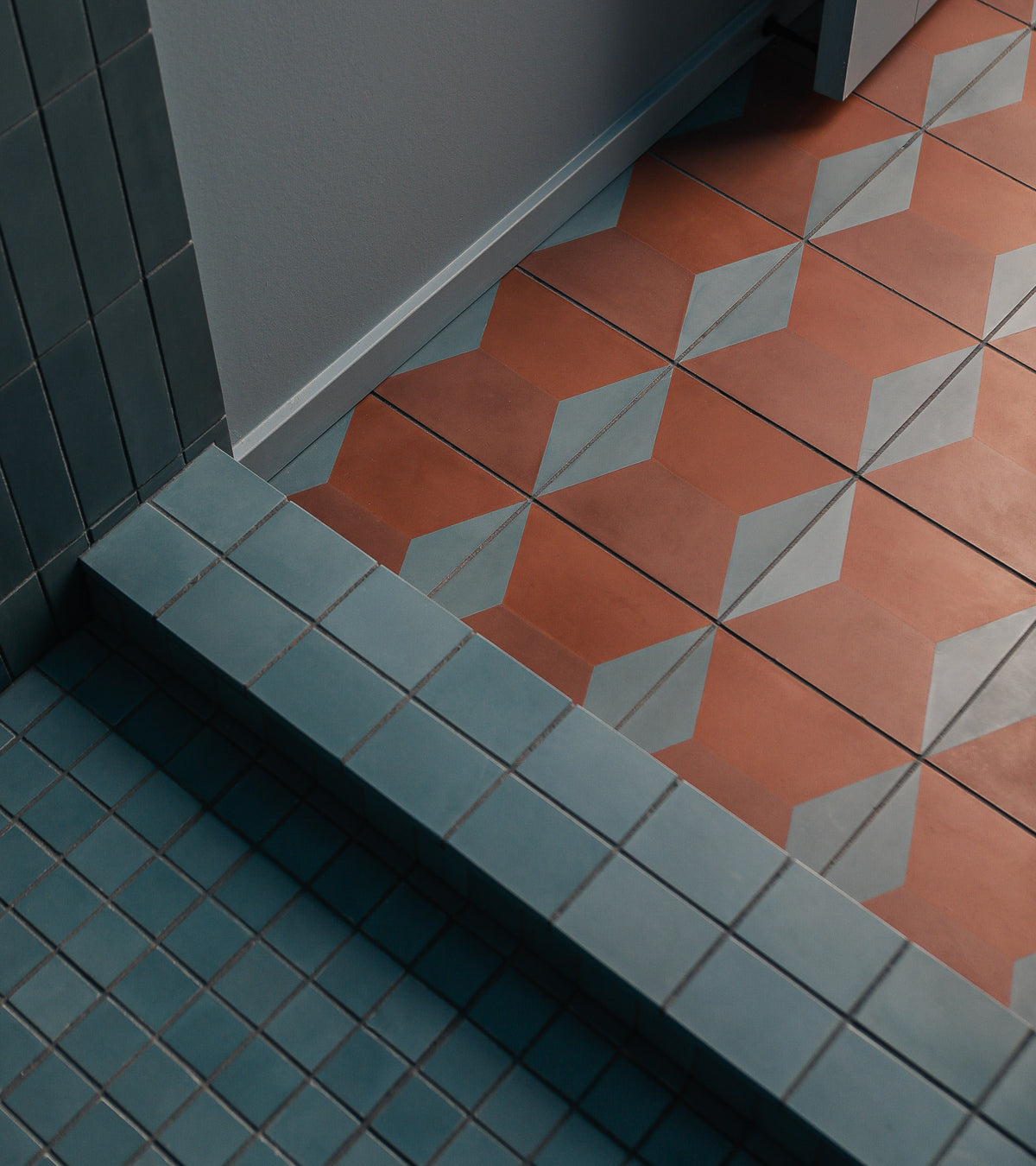 The lower floor has small square blue tiles; the upper step uses Zia Tile's Colorama Tyrian 8x8 handmade tiles—orange with a blue and white geometric diamond pattern. Walls are tiled in blue and painted white.