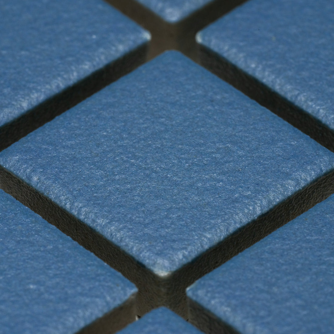 Close-up of Zia Tile’s Iconic Blue 1x1 ceramic tiles arranged diagonally. Textured, slightly rough surface and visible grout lines highlight the blue square design.
