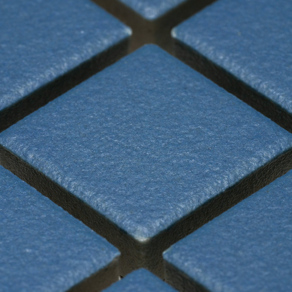 Close-up of Zia Tile’s Iconic Blue 1x1 ceramic tiles arranged diagonally. Textured, slightly rough surface and visible grout lines highlight the blue square design.
