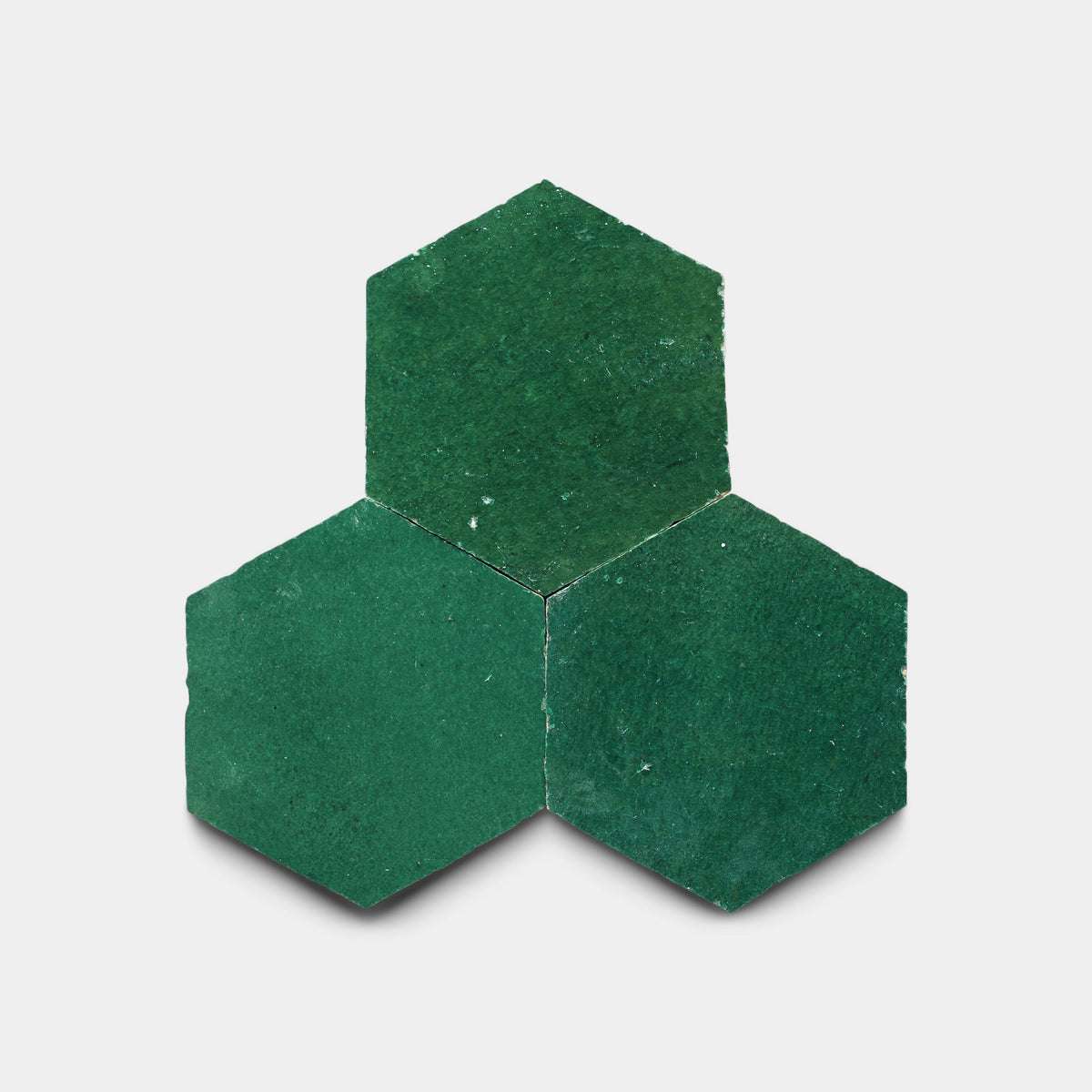 Three Jade Hex ceramic tile samples from Zia Tile, in dark green, are arranged with one on top and two below to form a cluster against a white background.