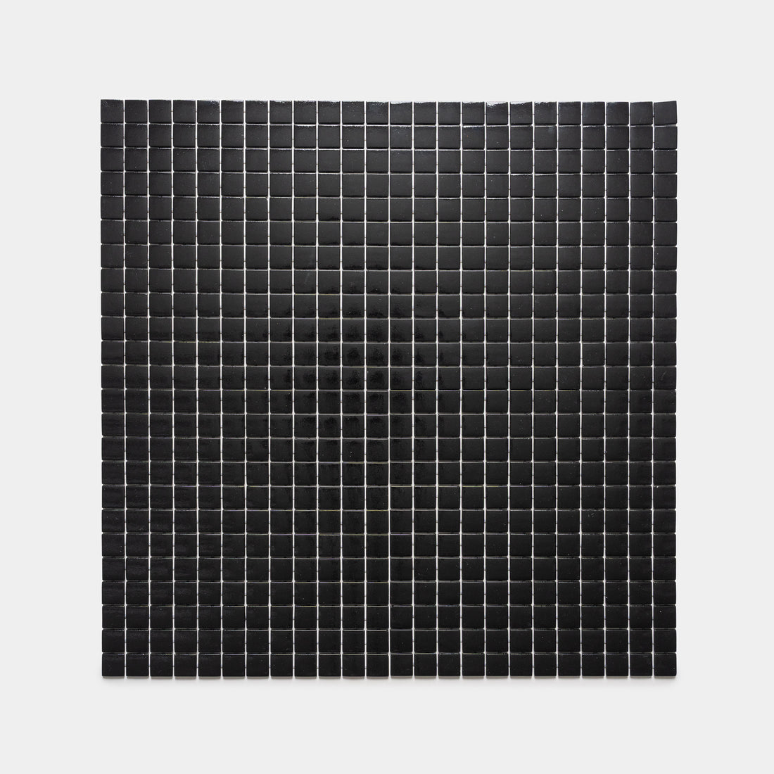 The Jet Black 1x1 by Zia Tile features small black squares arranged in neat rows and columns on a white background, enhanced by a subtle shadow or gradient that forms a faint dark circle at the center.