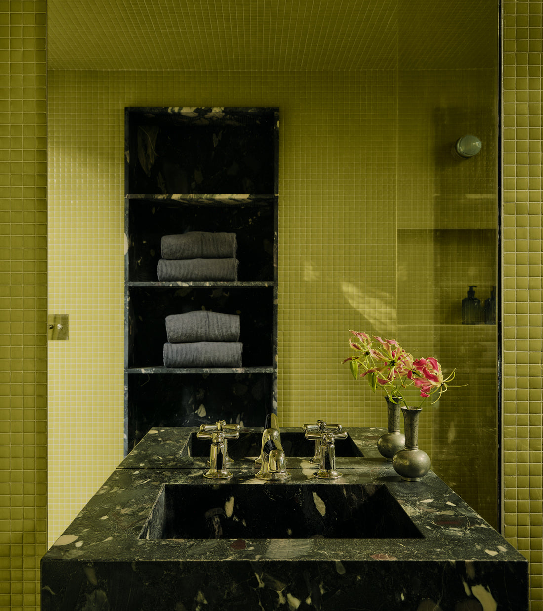 A bathroom vanity with a dark stone countertop and integrated sink, set against a wall of Kiwi 1x1 lime-green square tiles.