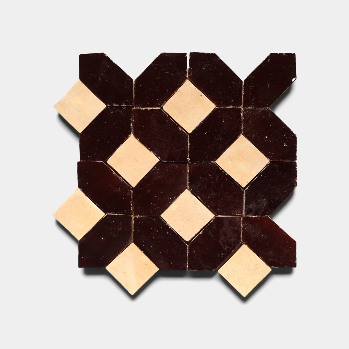 The Lattice 6 sample by Zia Tile features a geometric mosaic of dark brown connected diamonds with beige diamond shapes at the intersections, all set against a light cement tile background.