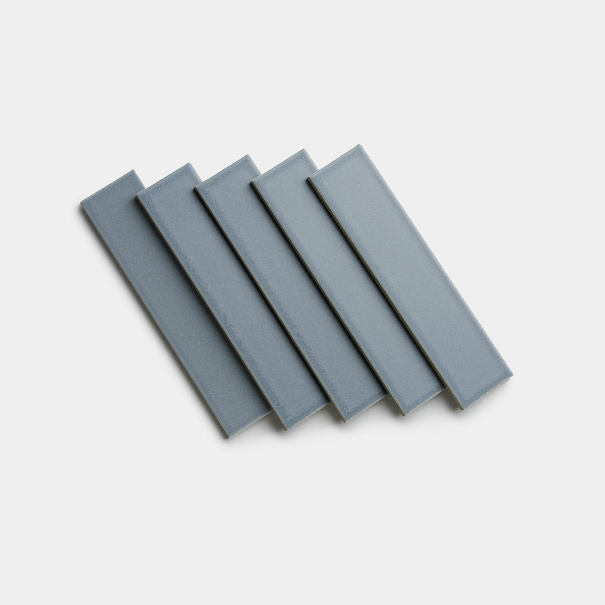 Five rectangular Loch 2x8 ceramic tiles by Zia Tile, featuring a glossy gray-blue finish, are arranged in a slightly fanned-out stack on a plain white background.