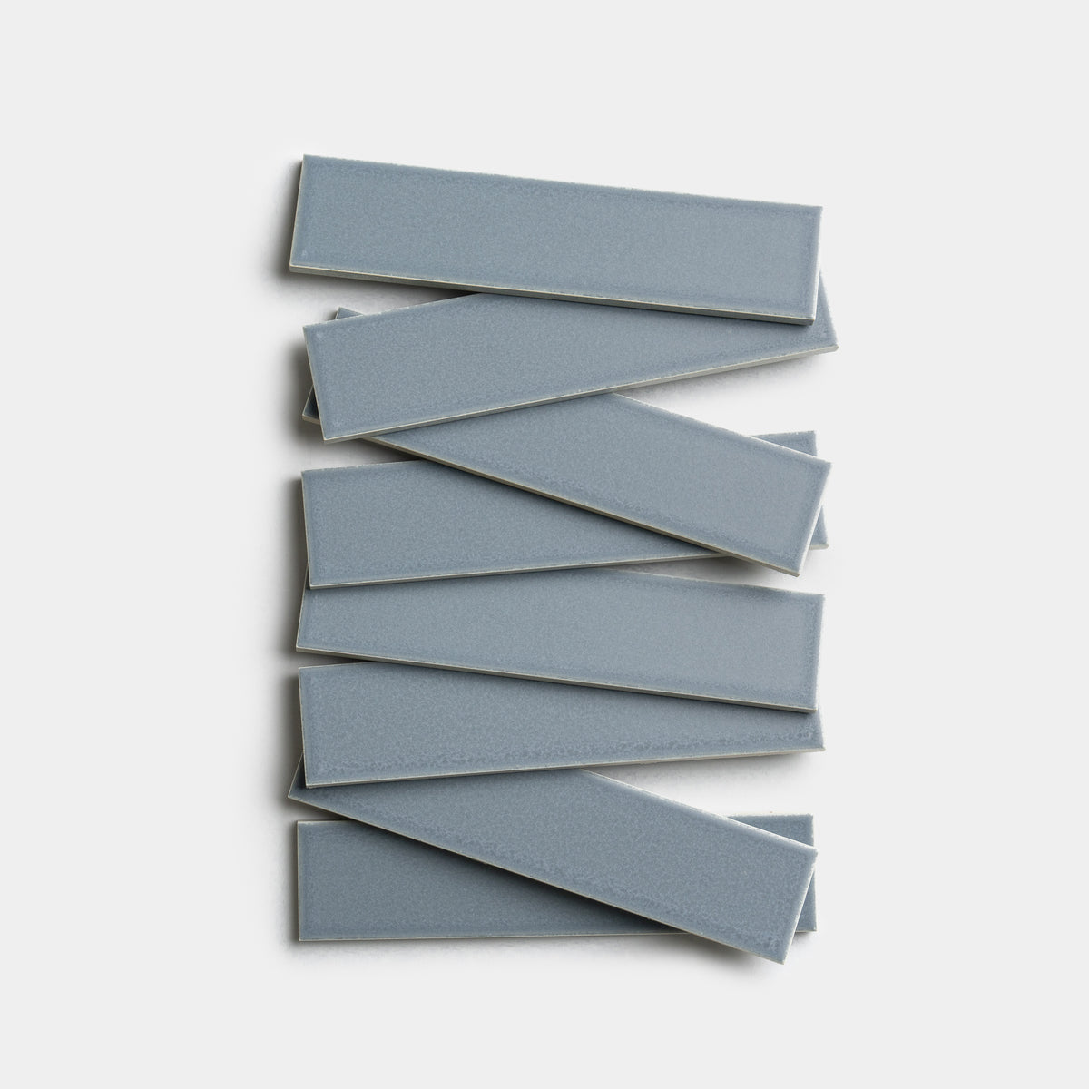 Nine Loch 2x8 rectangular blue-gray ceramic tiles by Zia Tile are stacked in a staggered, overlapping arrangement on a white background.