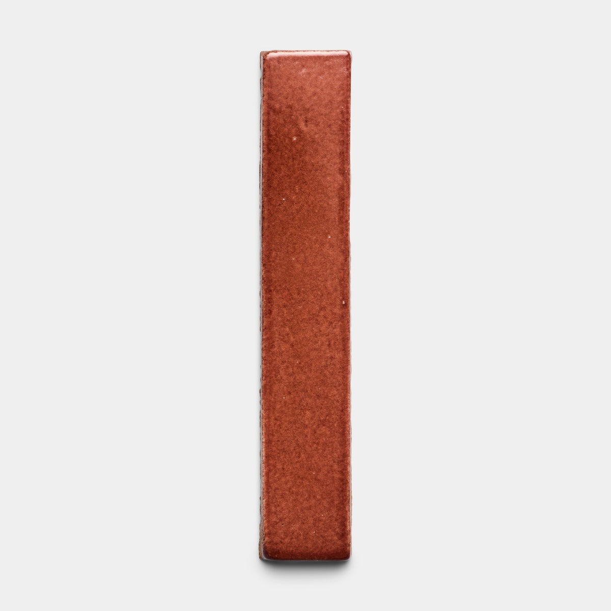 The Lupe Mini Bar by Zia Tile stands upright on a plain light gray background, its rectangular reddish-brown shape displayed from the narrow edge for a minimalistic look.