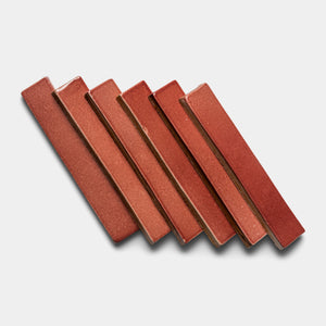 Six Lupe Mini Bar tiles by Zia Tile, rectangular and reddish-brown ceramic, are arranged diagonally in a staggered layout on a light gray background.