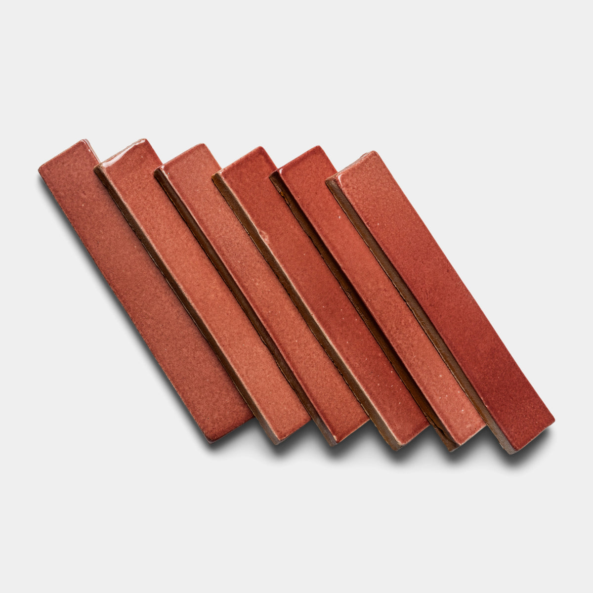 Six Lupe Mini Bar tiles by Zia Tile, rectangular and reddish-brown ceramic, are arranged diagonally in a staggered layout on a light gray background.