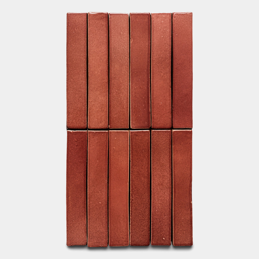Twelve Lupe Mini Bar tiles by Zia Tile, red and rectangular, are arranged vertically in two rows of six on a plain light gray background.