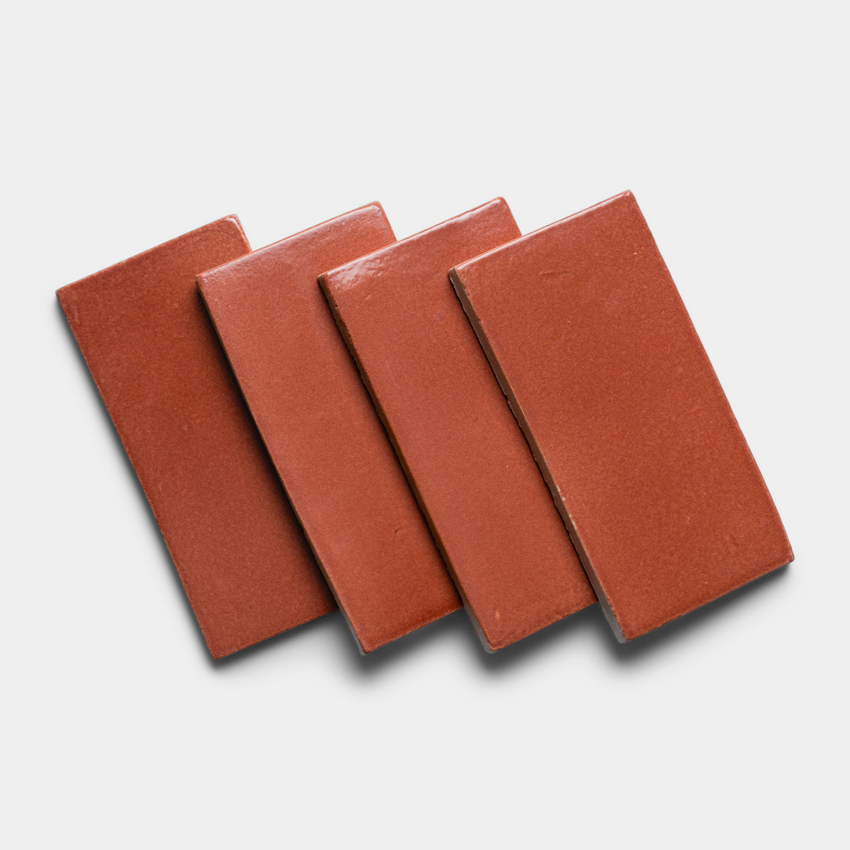Four Lupe 4x8 Rectangle tiles by Zia Tile, in a reddish-brown ceramic, are arranged in a slightly overlapping diagonal row on a white background.