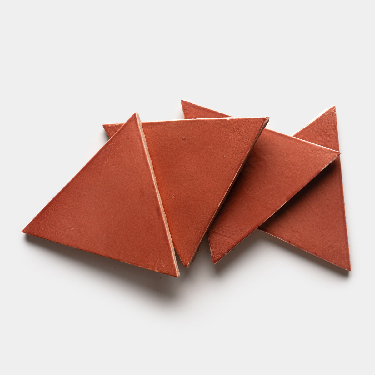 Four Lupe Triangle ceramic tiles by Zia Tile, featuring a reddish-brown hue and triangular shape, are overlapped on a plain white background.