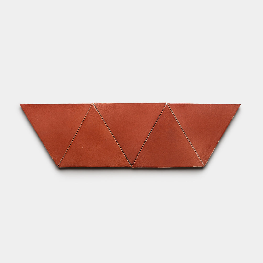 Six Lupe Triangle tiles by Zia Tile, in terracotta color, are arranged in a horizontal row to create a geometric zigzag pattern against a plain white background.