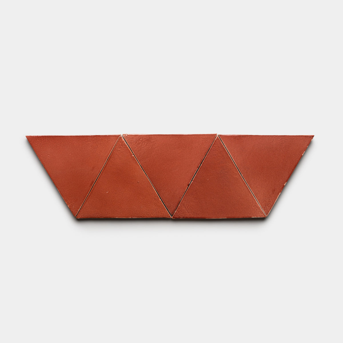 Six Lupe Triangle tiles by Zia Tile, in terracotta color, are arranged in a horizontal row to create a geometric zigzag pattern against a plain white background.