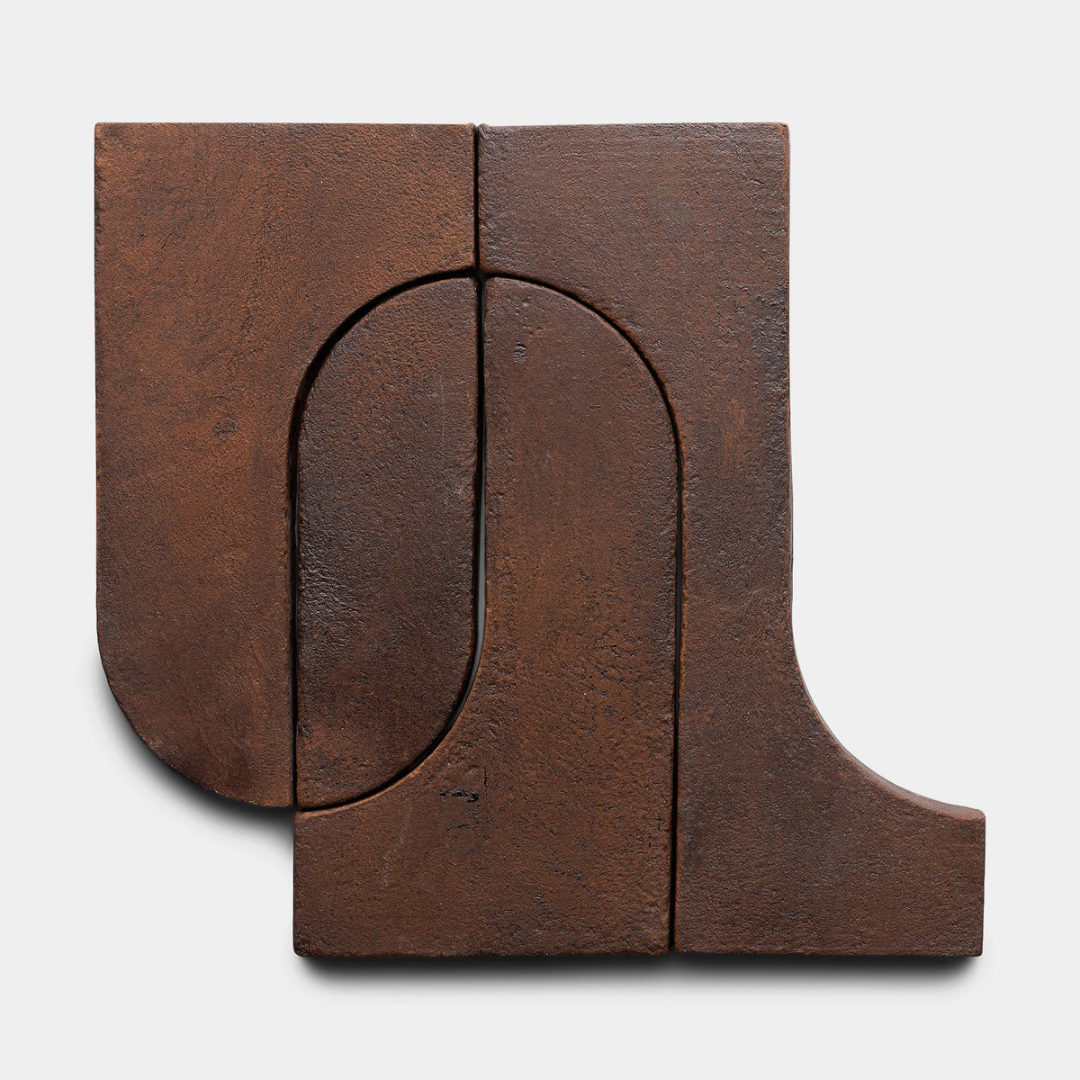 Durango + Madera, Sample by Zia Tile features three interlocking, rust-colored metal segments with textured surfaces forming abstract geometric shapes—both curved and straight—set against a white background.