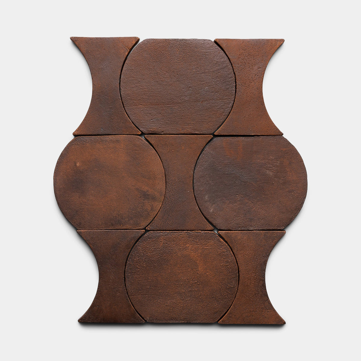 Six interlocking Oaxaca + Madera ceramic tiles by Zia Tile, in a rust color, create a geometric pattern of circles and hourglass shapes displayed on a plain, light background.