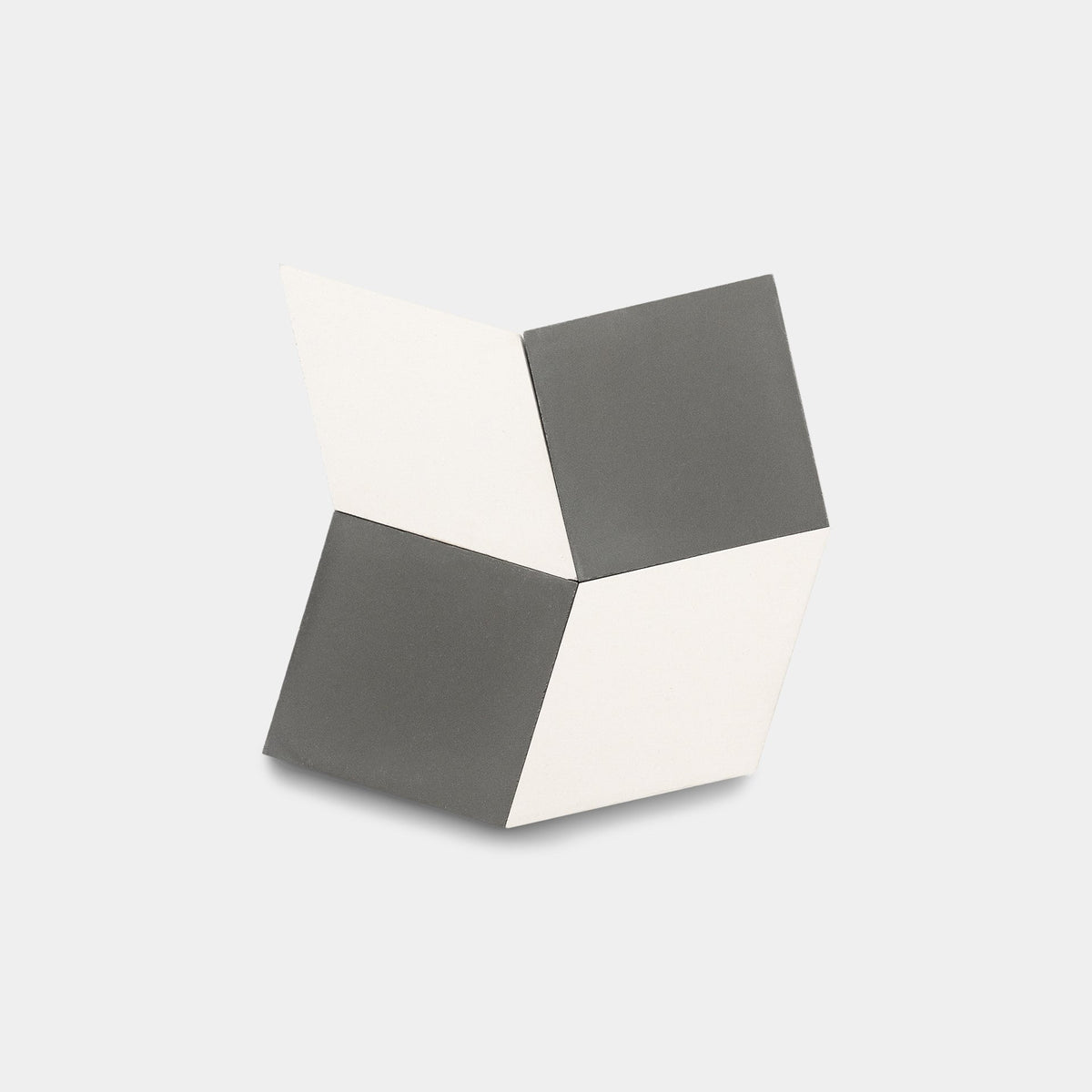The Madrid Ash + White sample by Zia Tile features four connected diamond-shaped panels—two white, two gray—arranged to create a 3D, optical illusion effect reminiscent of handmade tile against a plain background.
