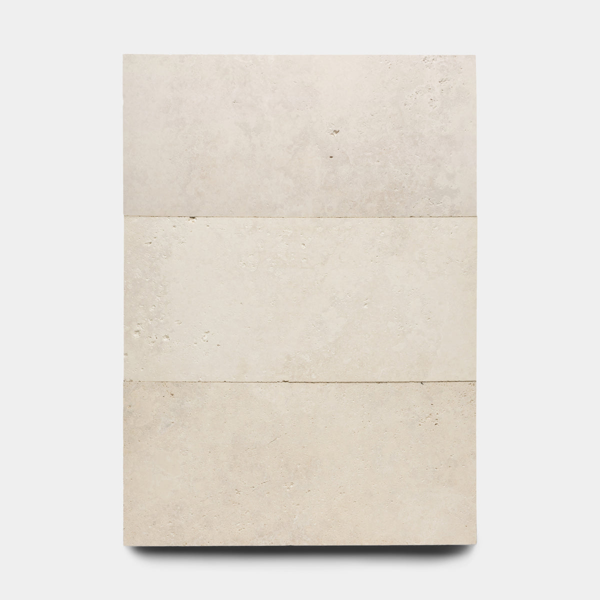 Three Mesa 12x24 rectangular beige tiles from Zia Tile are stacked vertically against a plain white background, showcasing subtle natural texture and slight color variations.