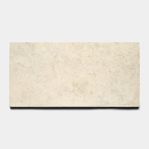 The Mesa 12x24 by Zia Tile is a rectangular, light beige Mexican Cantera stone tile with a smooth, slightly textured surface, shown against a plain white background.
