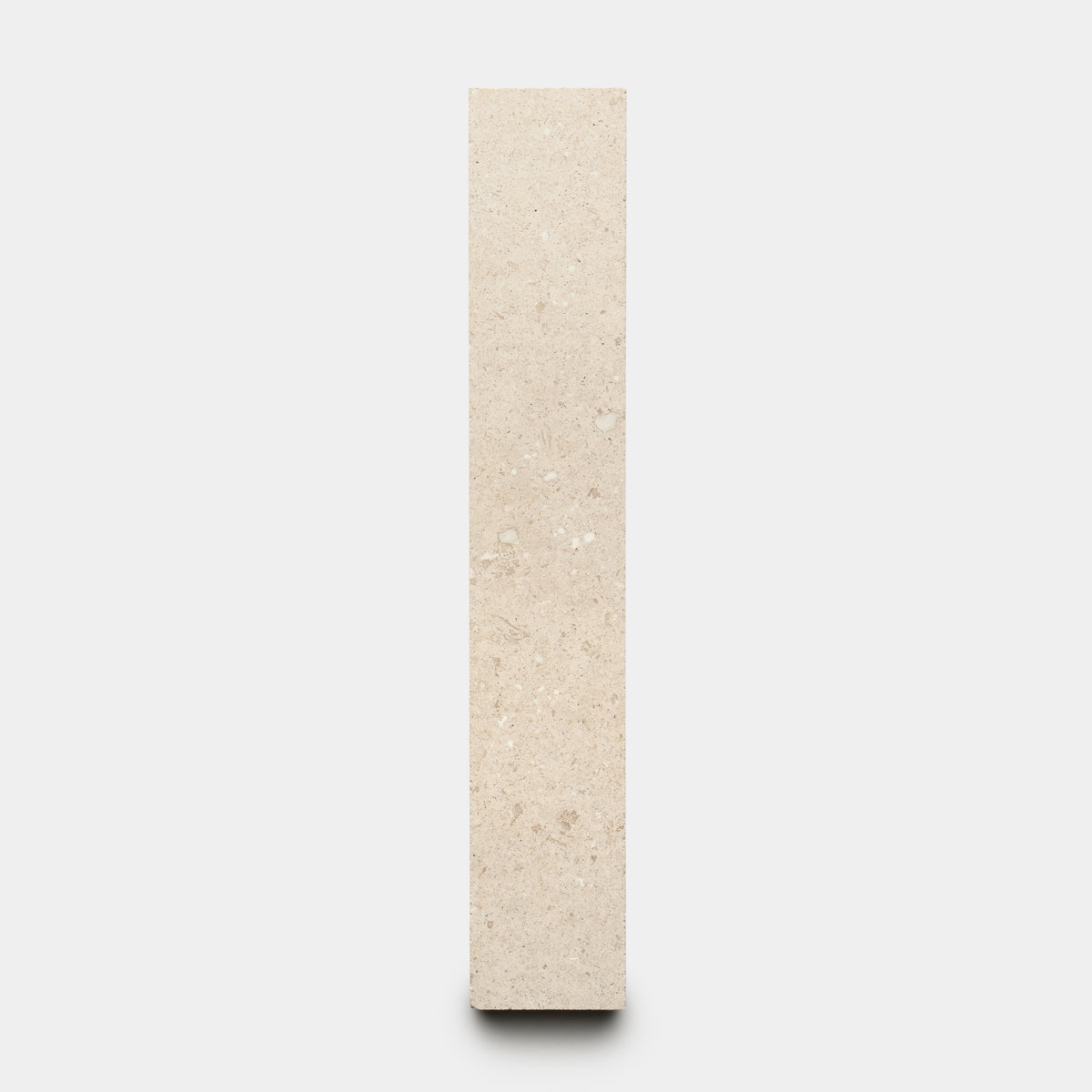 The Mesa 2x12 by Zia Tile is a vertical, rectangular beige stone slab with a smooth surface and subtle natural speckles, shown standing upright against a plain white background.