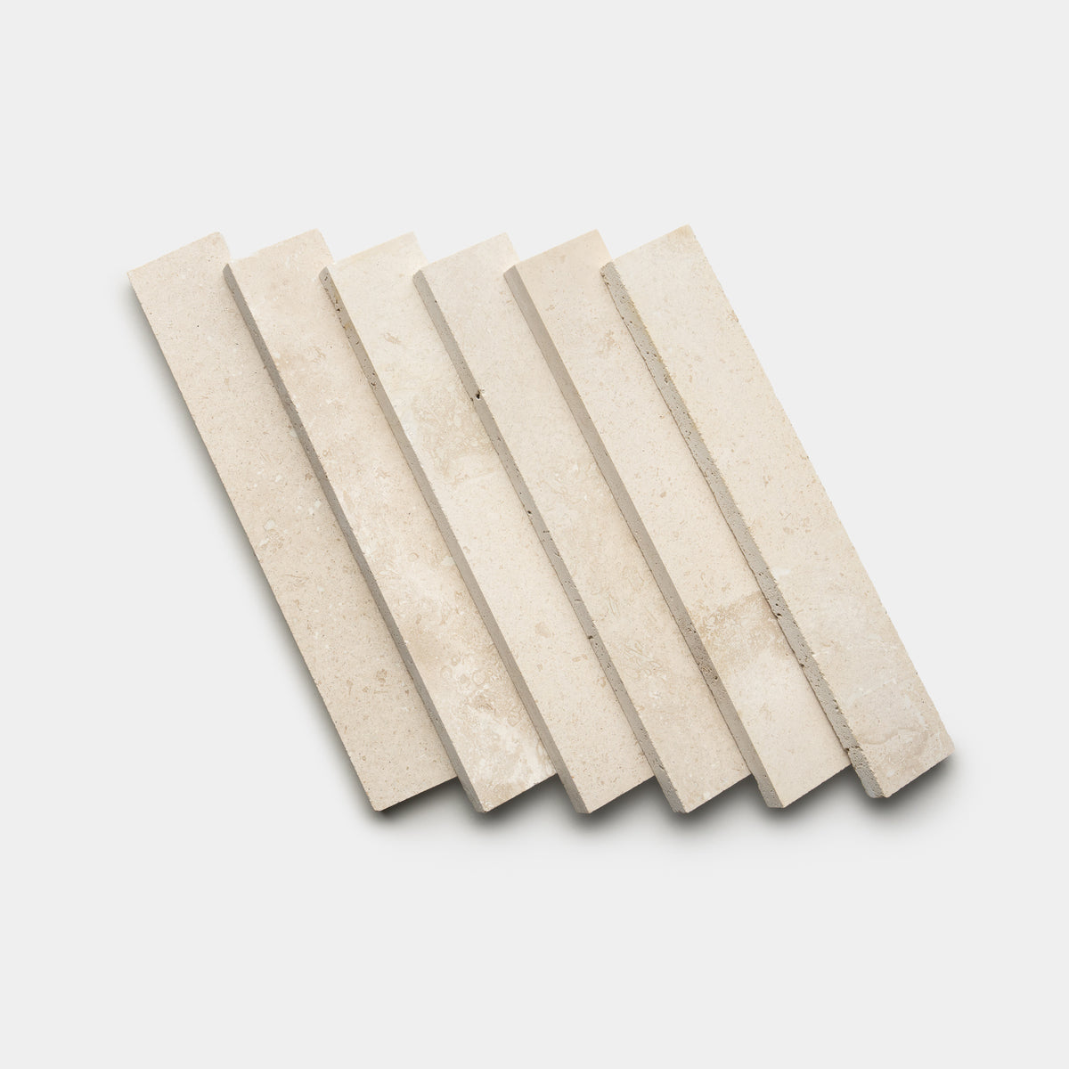 Six Mesa 2x12 rectangular beige stone tiles from Zia Tile are arranged diagonally in a staggered, overlapping pattern on a white background.
